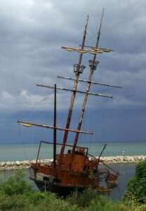 The rusted, fire-damaged hull of the La Grande Hermine schooner replica sitting in the shallow water of Jordan Harbour at Jordan Station, Ontario.