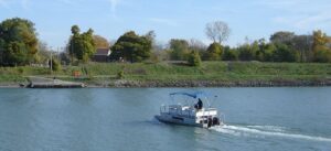 A small passenger ferry crossing the Welland Canal, approaching the tree-lined east bank at Port Robinson, Ontario.