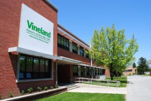 Red-brick main office building of the Vineland Research and Innovation Centre in Vineland, Ontario, with a wheelchair-accessible ramp and landscaped entrance under a clear sky.
