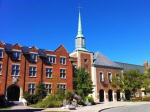 The stone collegiate-gothic Upper School building of Ridley College, with its central tower and arched entrance, set among lawns and trees in the Western Hill neighbourhood of St. Catharines, Ontario.